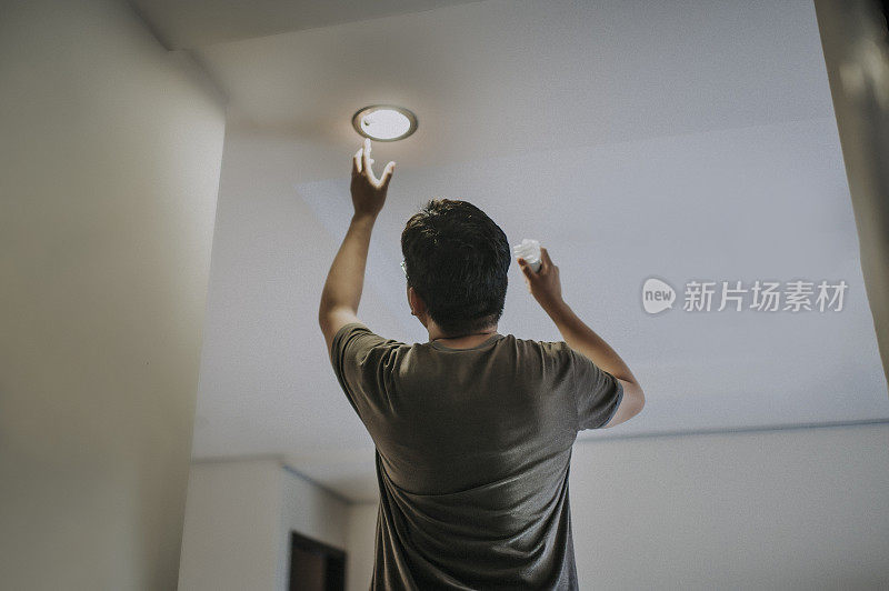 an asian chinese mid adult male changing light bulb in living room, apartment home